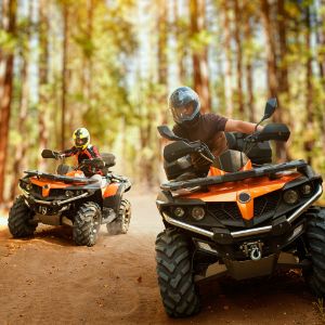 Two Quad Bikes and riders driving through forest.