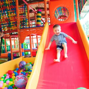 child sliding odwn a red slide with ball pit in the background