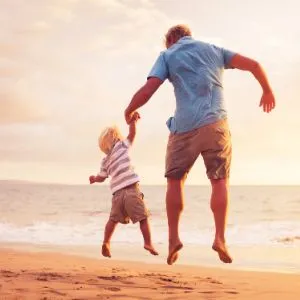 Man and small child jumping for joy on a beach
