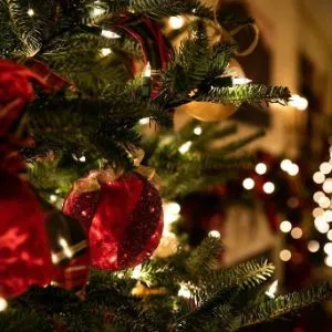 girl in a red jumper hanging a bauble on a Christmas tree.