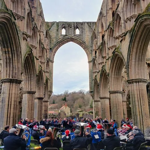 people sitting in the ruins of Rievaulx abbey watching a brass band play