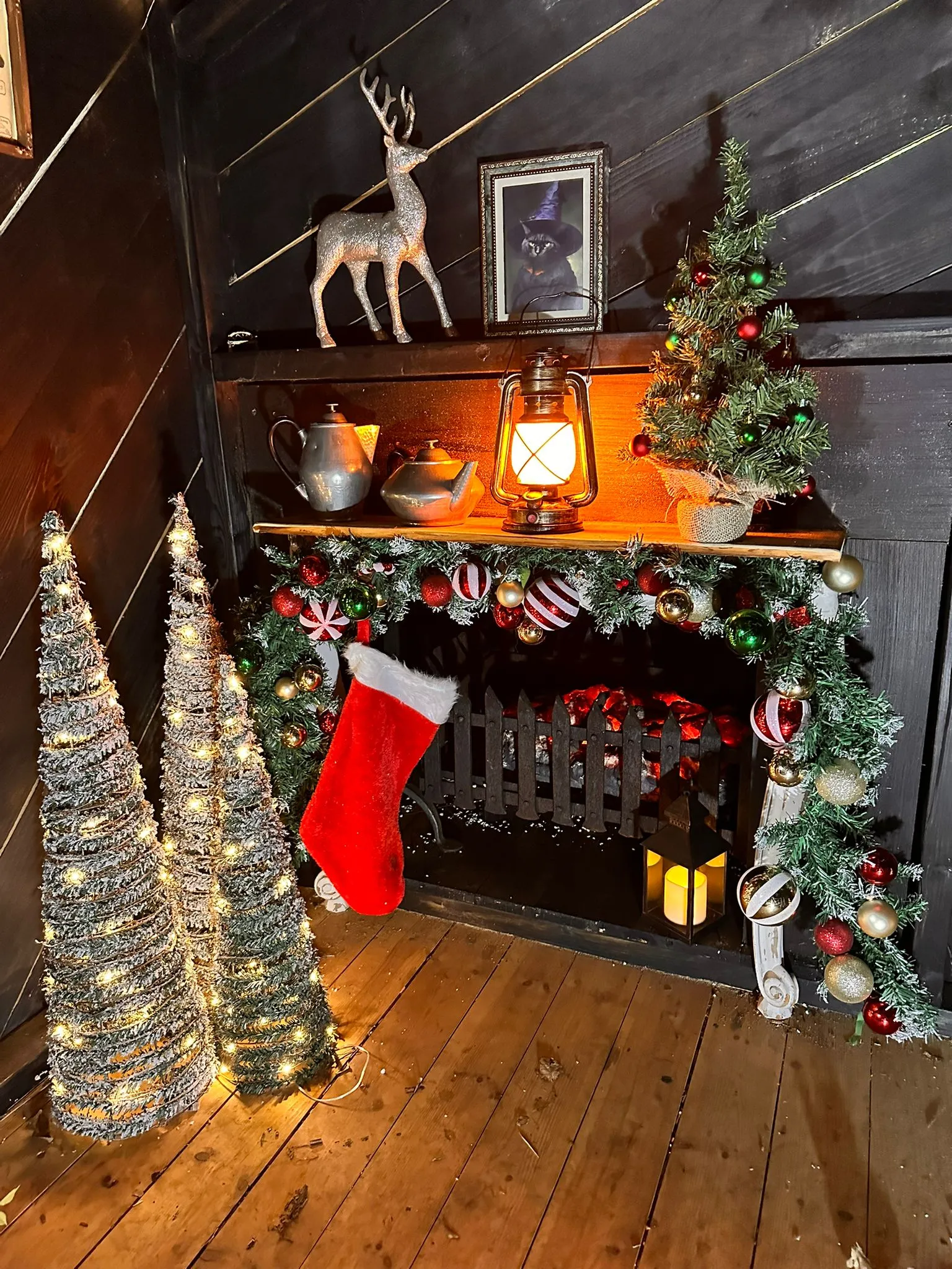 Fireplace ina wooden cabin decorated with stockings, small christmas trees and other decorations.
