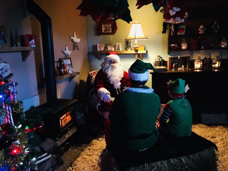 Two elves sitting with Father Christmas in his grotto 