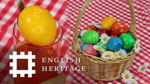 Small bsket of decorated eggs to the left on a red and white gingham tablecloth with a large yellow egg to the right.  English heritage text and logo to the bottom left left,