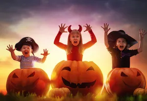 Three children on mock scary poses appearing from behind large pumpkins