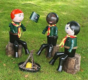 three cub scouts made from flower pots sitting on logs around a campfire