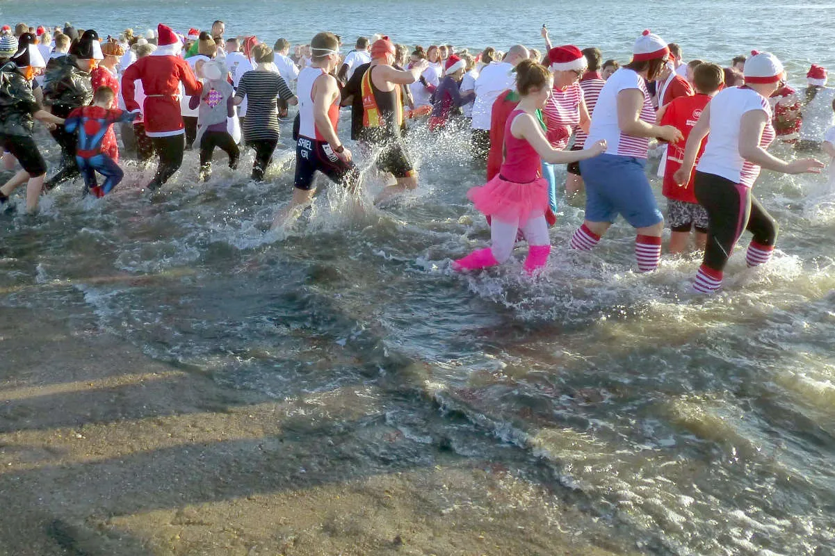 people running into the sea, some in fancy dress, many wearing santa hats