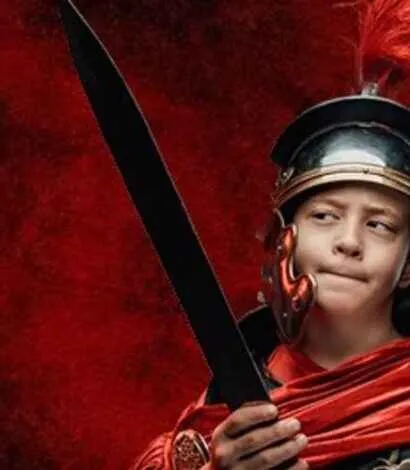 Child dressed as a roman centurion with a sword, red background.