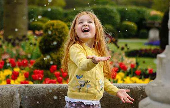small child in a yellow jumper laughing at bubbles in an outdoor setting