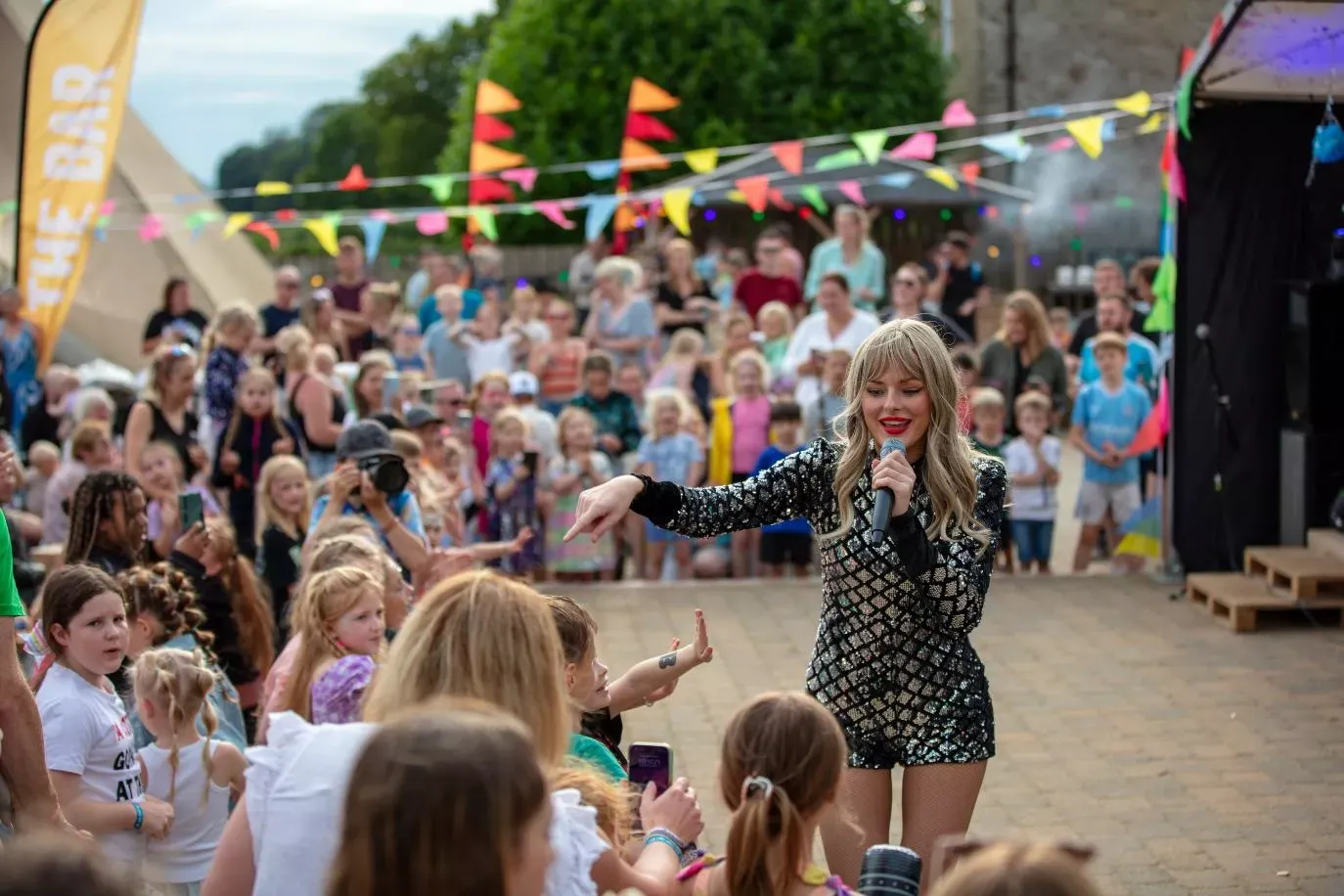 singler in a sparkly dress giving high foves to children around the stage