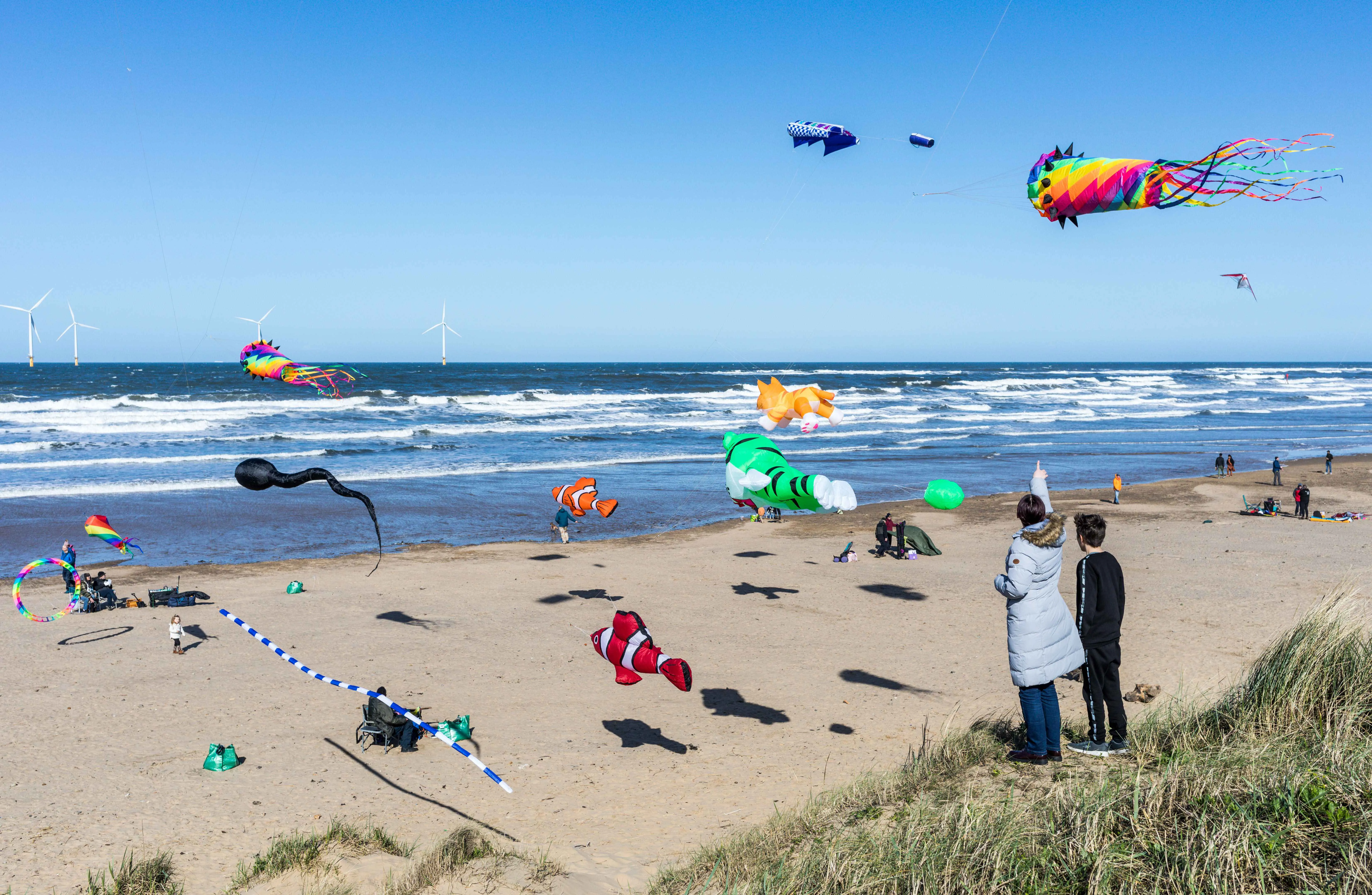 two people watching a series of kites flying above the beach