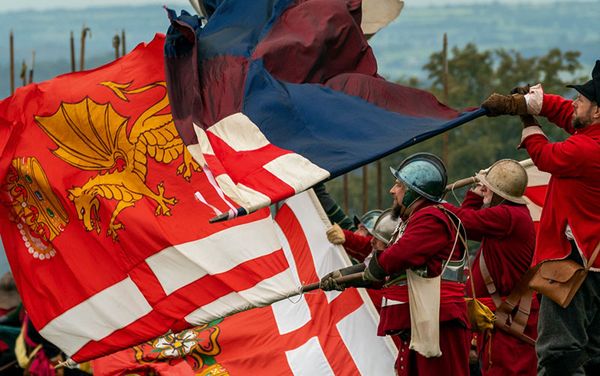 re-enactors in englich civil war uniforms with flags in bright colours