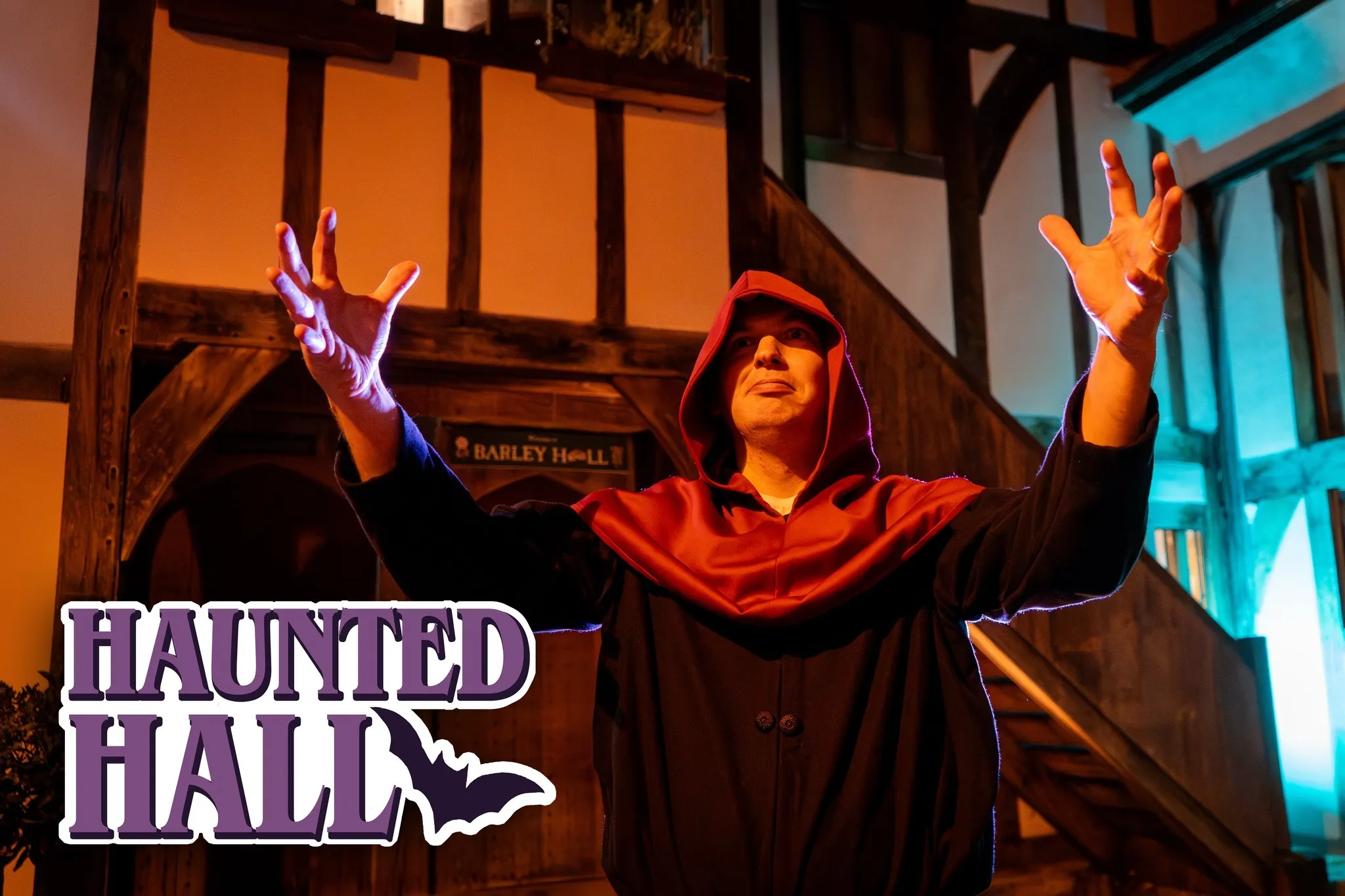 man in a black cloak with a red hood standing with his arms raised and forward.