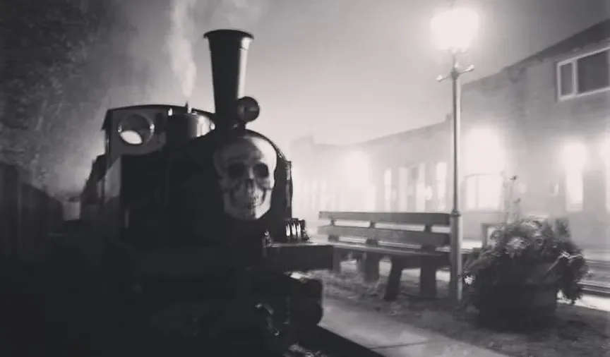 black and white image os a train with a skull face on a smoke filled platform