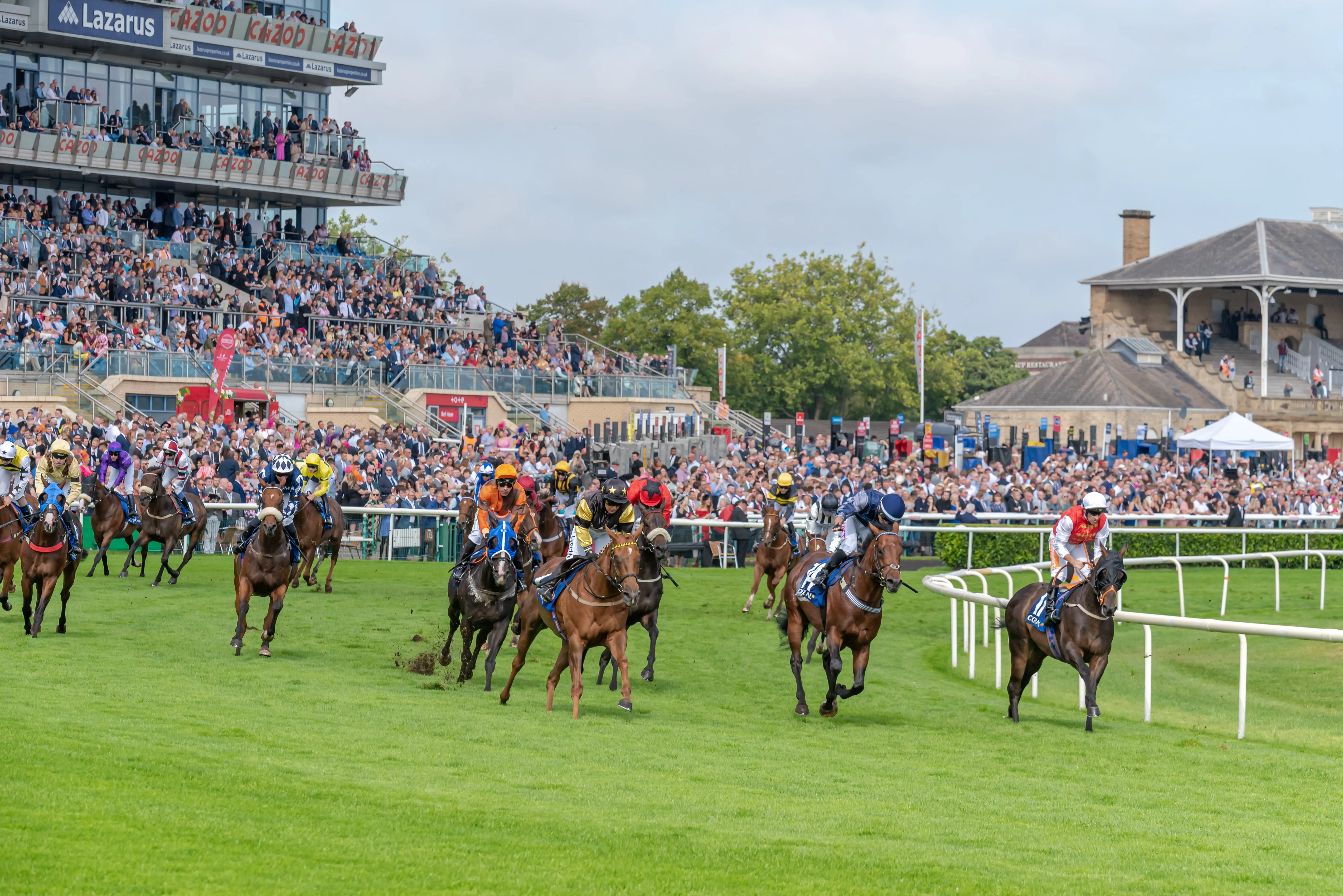 racehorses rounding a bend at a racetrack with a stadium in the background